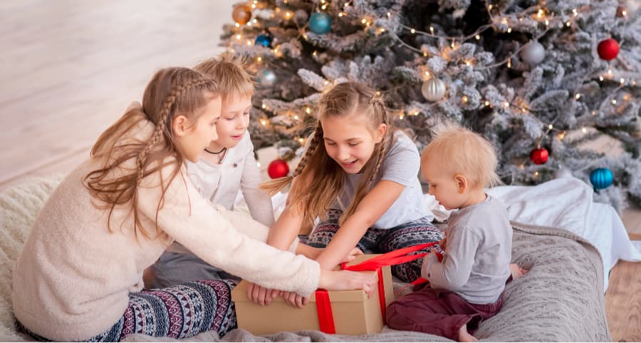 Siblings opening a gift in the living room near a Christmas tree.